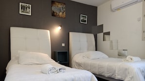 Habitación de hotel con dos camas, cada una con cabecero, mesita de noche y aire acondicionado de pared.