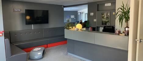 A reception area with a grey and red seating area, a reception desk, a television, and a sign indicating the location of the toilets.
