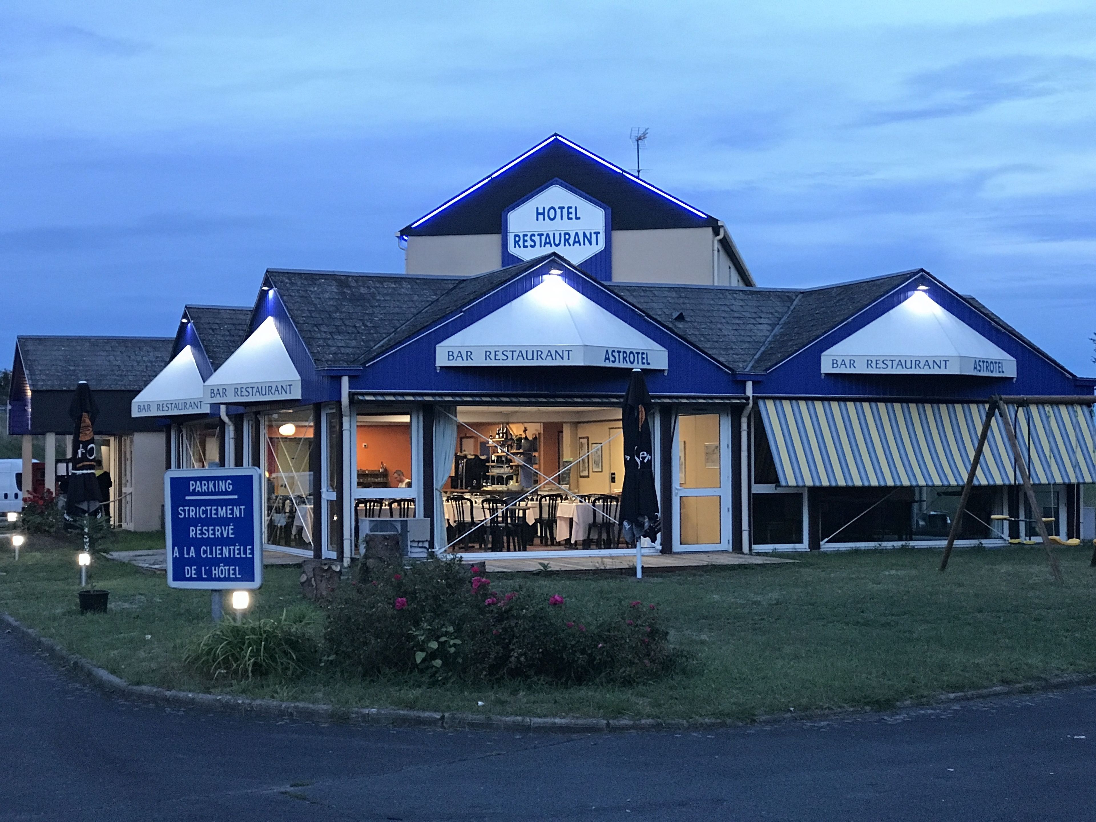 A hotel with a restaurant and bar, featuring a blue and white color scheme, outdoor seating, and a parking sign.