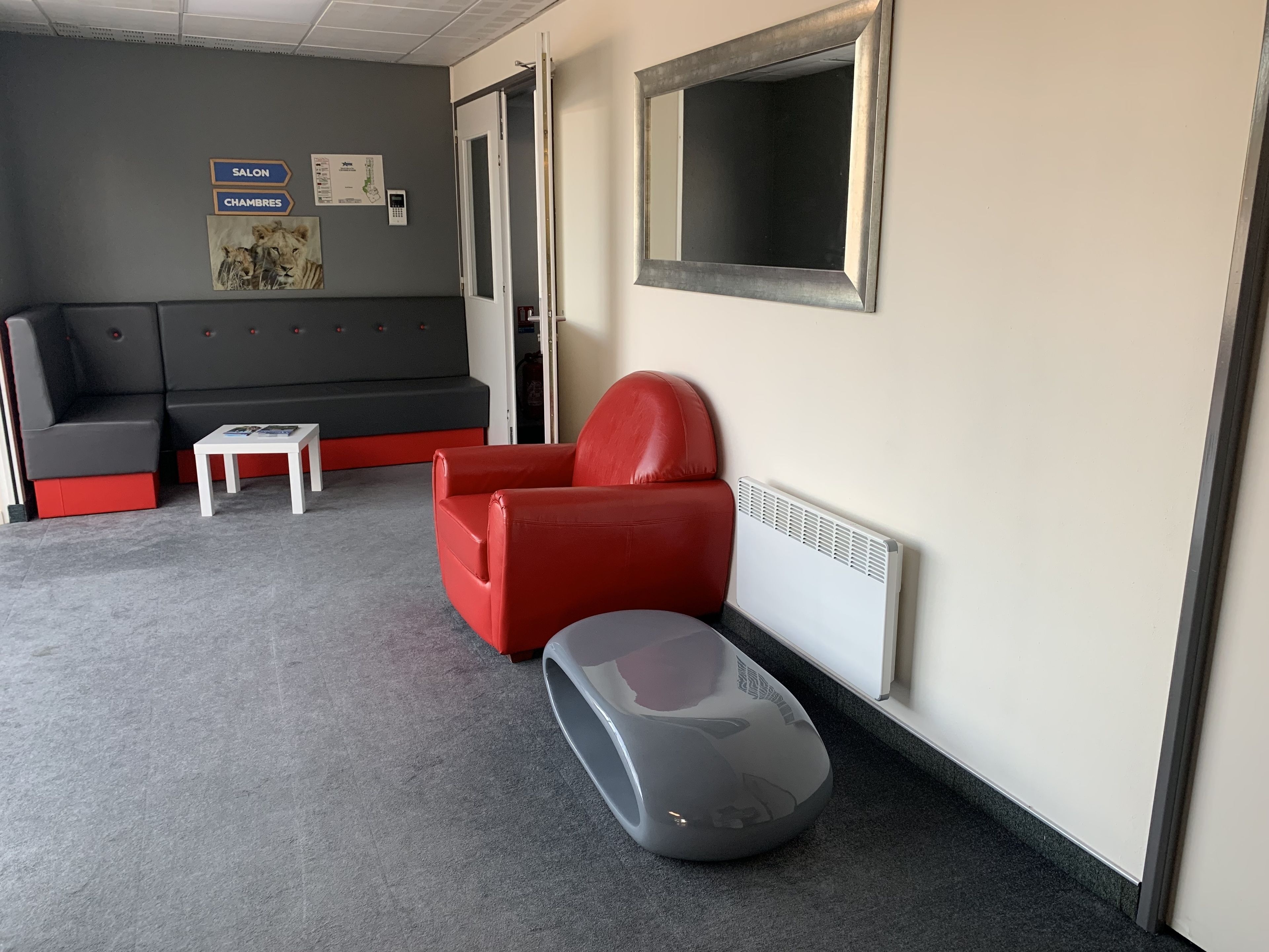 Ein modernes Zimmer mit einem grauen Sofa, einem roten Sessel, einem kleinen weißen Tisch und einem grauen Koffer auf dem Boden.
