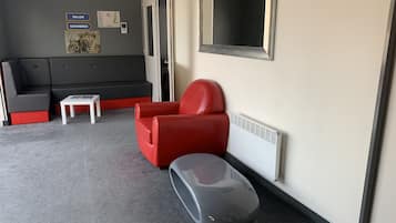 A modern room with a grey sofa, a red chair, a small white table, and a grey suitcase on the floor.