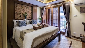 Habitación de hotel con una cama grande, cabecera de madera con detalles florales tallados, balcón con vistas y techo con iluminación empotrada.