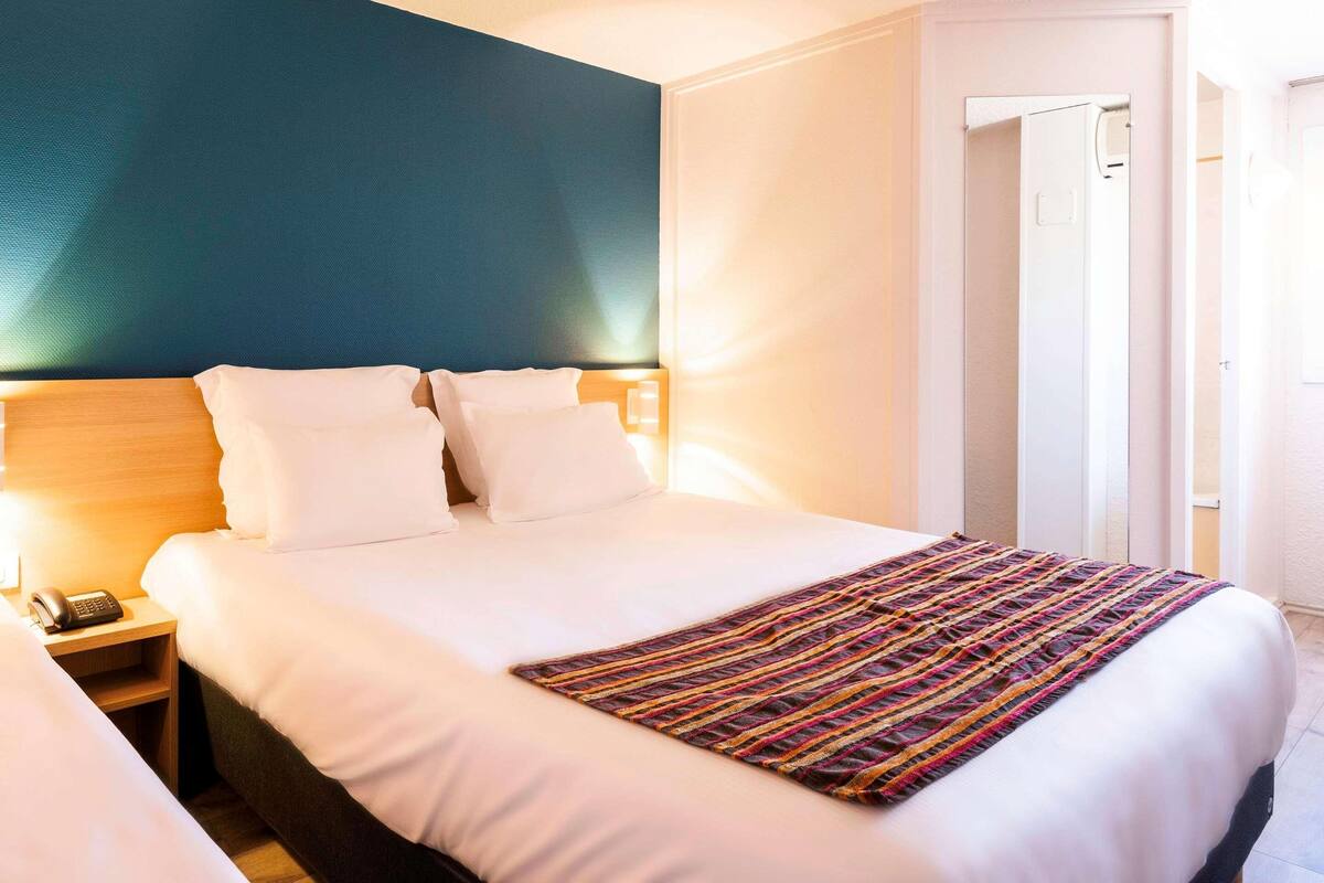 Une chambre d’hôtel avec un grand lit, une table de chevet avec un téléphone et une porte donnant sur une autre pièce.
