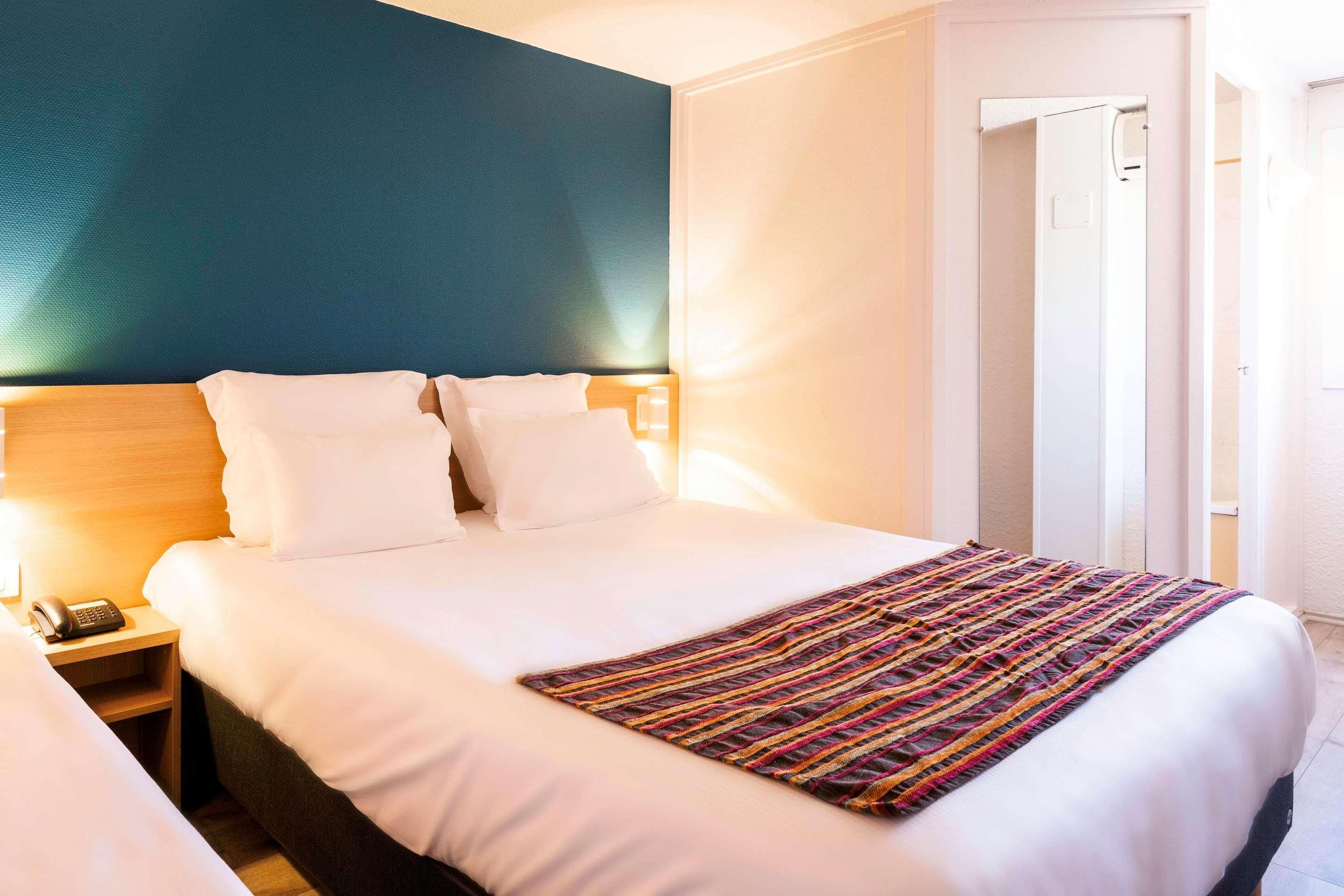A hotel room with a large bed, a bedside table with a phone, and a door leading to another room.