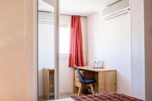 Una habitación pequeña y luminosa con un escritorio de madera, una silla, una cama y una ventana con cortina roja.