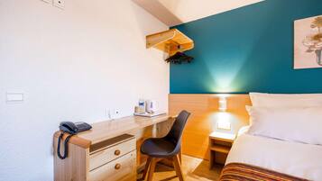 Een hotelkamer met een bed, een bureau met telefoon, een stoel, een nachtkastje met lamp en een wandkapstok.