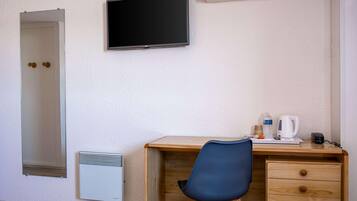 Habitación de hotel con un escritorio de madera, una silla, televisor montado en la pared, radiador y dispensador de agua.
