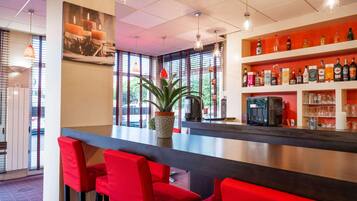 A bar area with red chairs, a potted plant, and shelves stocked with bottles and glasses.