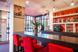 Una zona de bar con sillas rojas, una planta en maceta y estantes llenos de botellas y vasos.