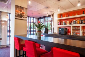 Una zona de bar con sillas rojas, una planta en maceta y estantes llenos de botellas y vasos.