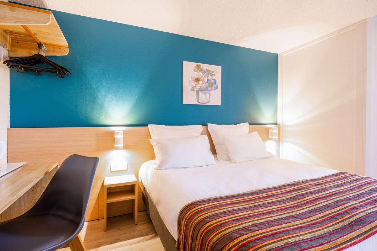 Une chambre d’hôtel avec un grand lit, un bureau avec une chaise, une petite table et un porte-manteau fixé au mur.