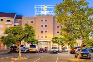 Un Comfort Hotel con vista despejada al estacionamiento, varios coches y árboles.