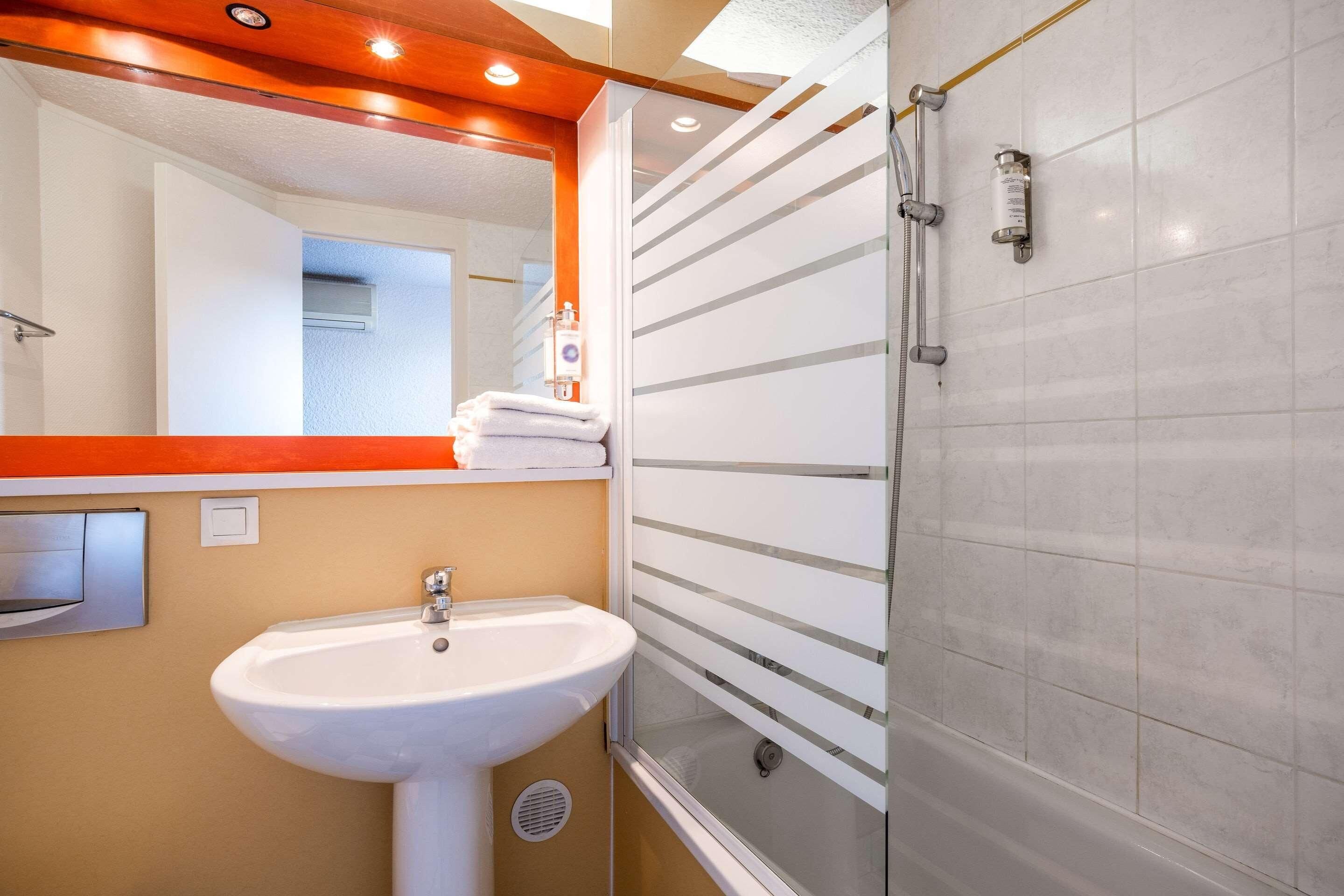 Une salle de bain avec un lavabo blanc, une cabine de douche en verre et un miroir avec un cadre en bois.
