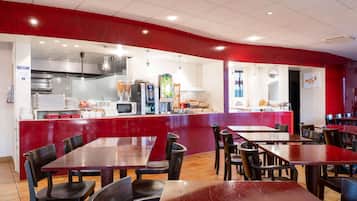 A restaurant with red walls, a kitchen area, and multiple tables and chairs.