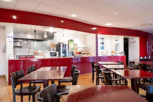 Un restaurante con paredes rojas, una zona de cocina y varias mesas con sillas.