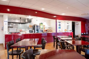Un restaurant aux murs rouges, avec un espace cuisine et de nombreuses tables et chaises.