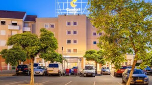 Un hôtel Comfort offrant une vue dégagée sur le parking, avec de nombreuses voitures et des arbres.