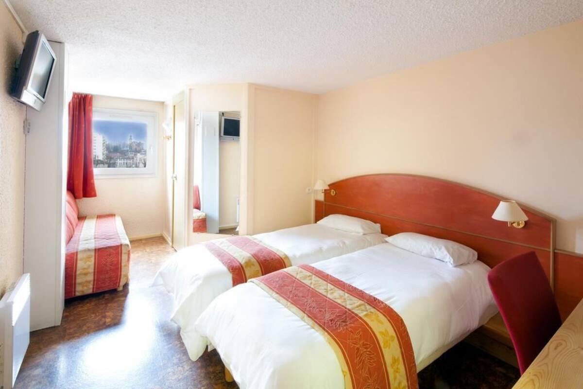 Une chambre d’hôtel avec deux lits, une télévision, une fenêtre donnant sur un beau paysage et un fauteuil rouge.