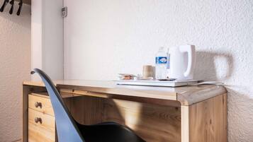 A wooden desk with a black chair, a white coffee maker, a bottle of water, and a cup.