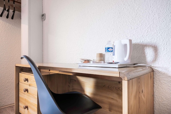 A wooden desk with a black chair, a white coffee maker, a bottle of water, and a cup. - Comfort Hotel Montlucon (Montlucon)