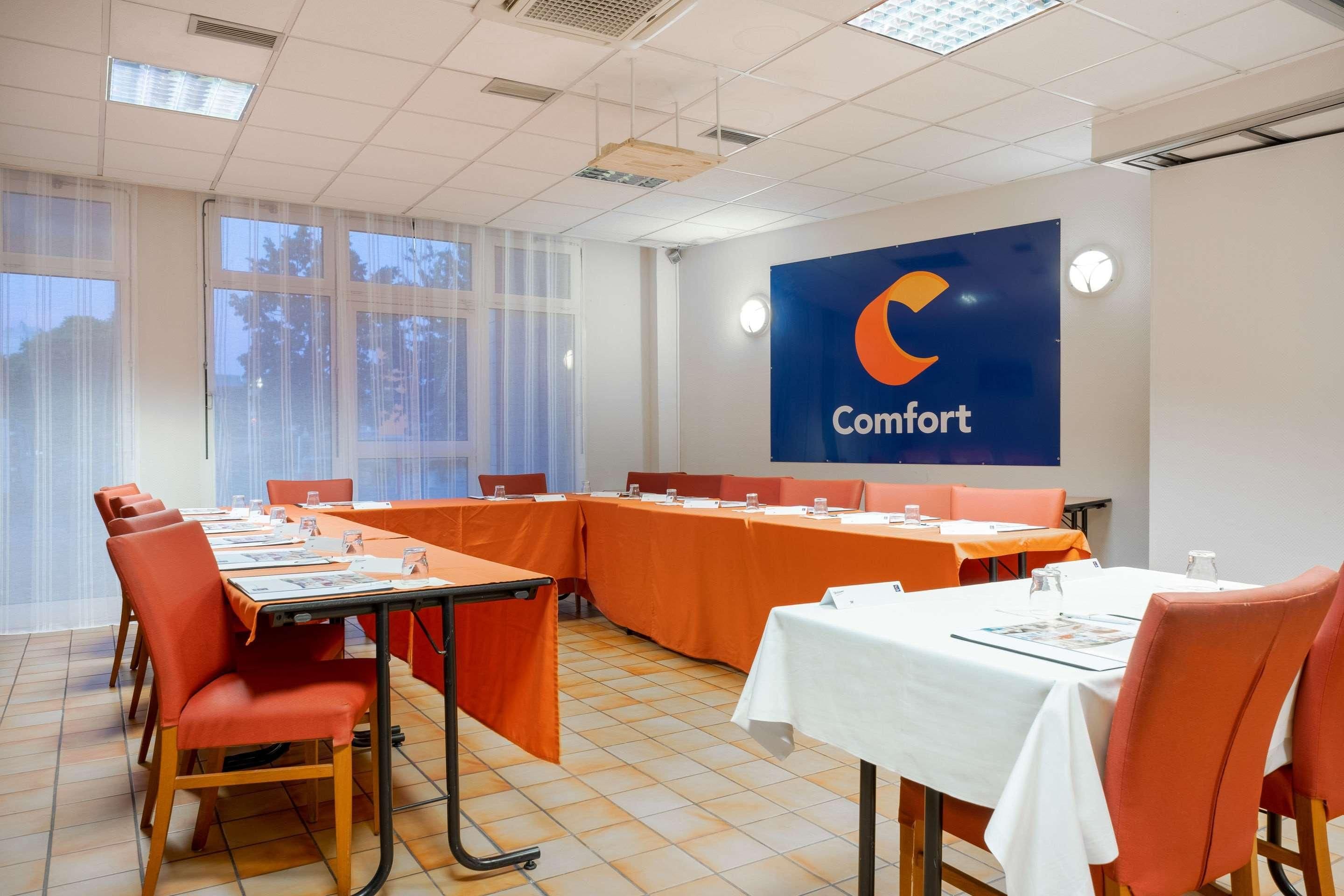 A conference room with a long table, orange chairs, and a large blue banner with the word "Comfort" on the wall.