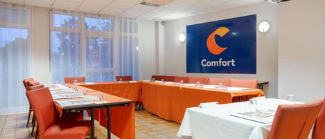 A conference room with a long table, orange chairs, and a large blue banner with the word "Comfort" on the wall.