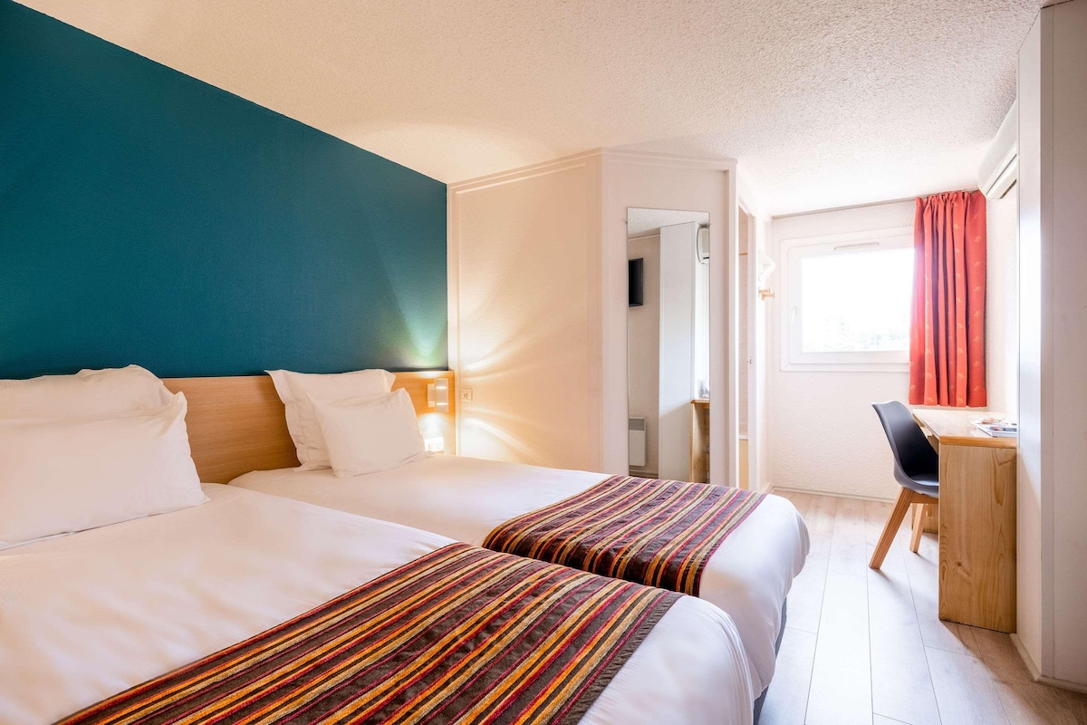 Une chambre d’hôtel avec deux lits, un bureau et une fenêtre avec des rideaux.