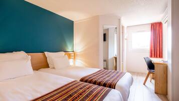 Habitación de hotel con dos camas, un escritorio y una ventana con cortinas.