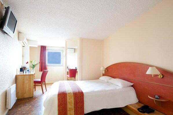 Una habitación de hotel con cama, escritorio, silla, televisor y ventana.