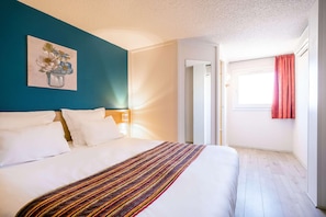 A hotel room with a bed, a painting on the wall, and a window with curtains. - Comfort Hotel Montlucon (Montlucon)