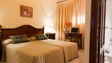 A hotel room with a large bed, a desk, a chair, a lamp, and a painting on the wall.