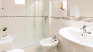 A bathroom with a glass-enclosed shower, a bidet, a sink, and a mirror.