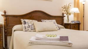 A neatly made bed with a floral pillow, a folded towel, and a small card on the bed.