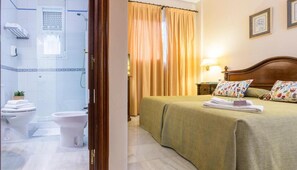 Hotelkamer met een bed, een badkamer met toilet en douche, en een raam met gordijnen.