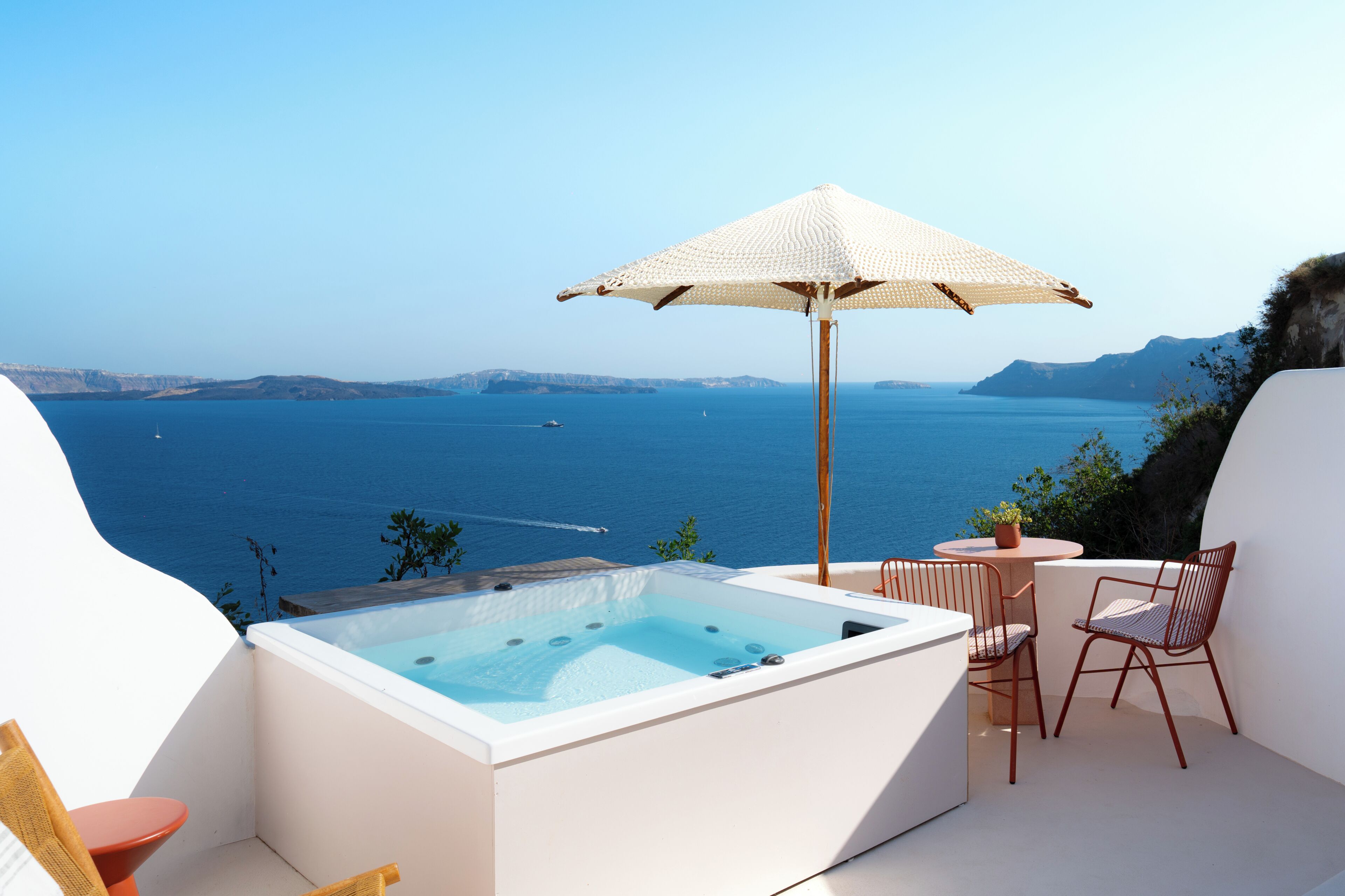 A hot tub with a view of the sea, a table with chairs, and an umbrella.