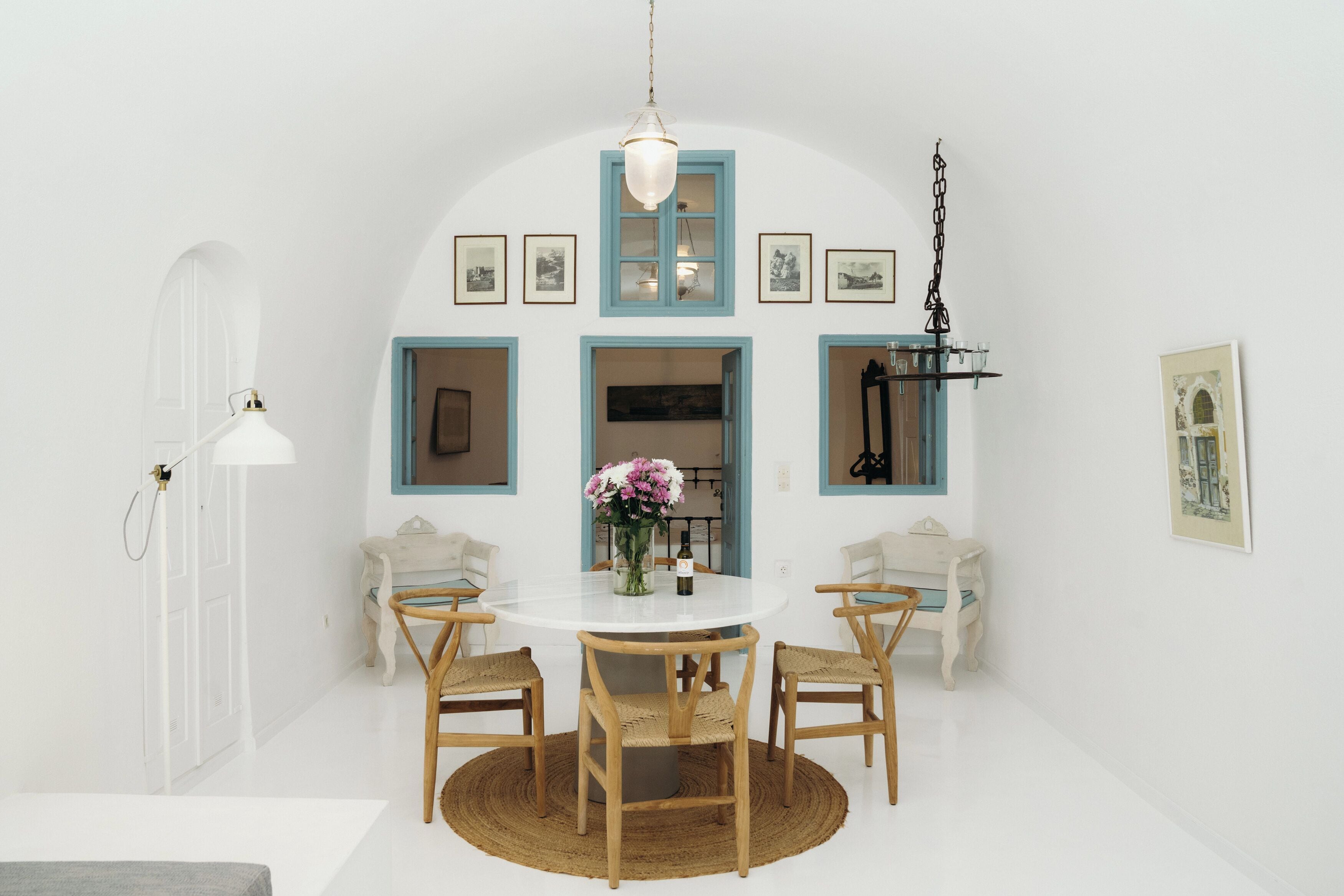 A dining area with a round table, four chairs, a vase with flowers, and framed pictures on the walls.