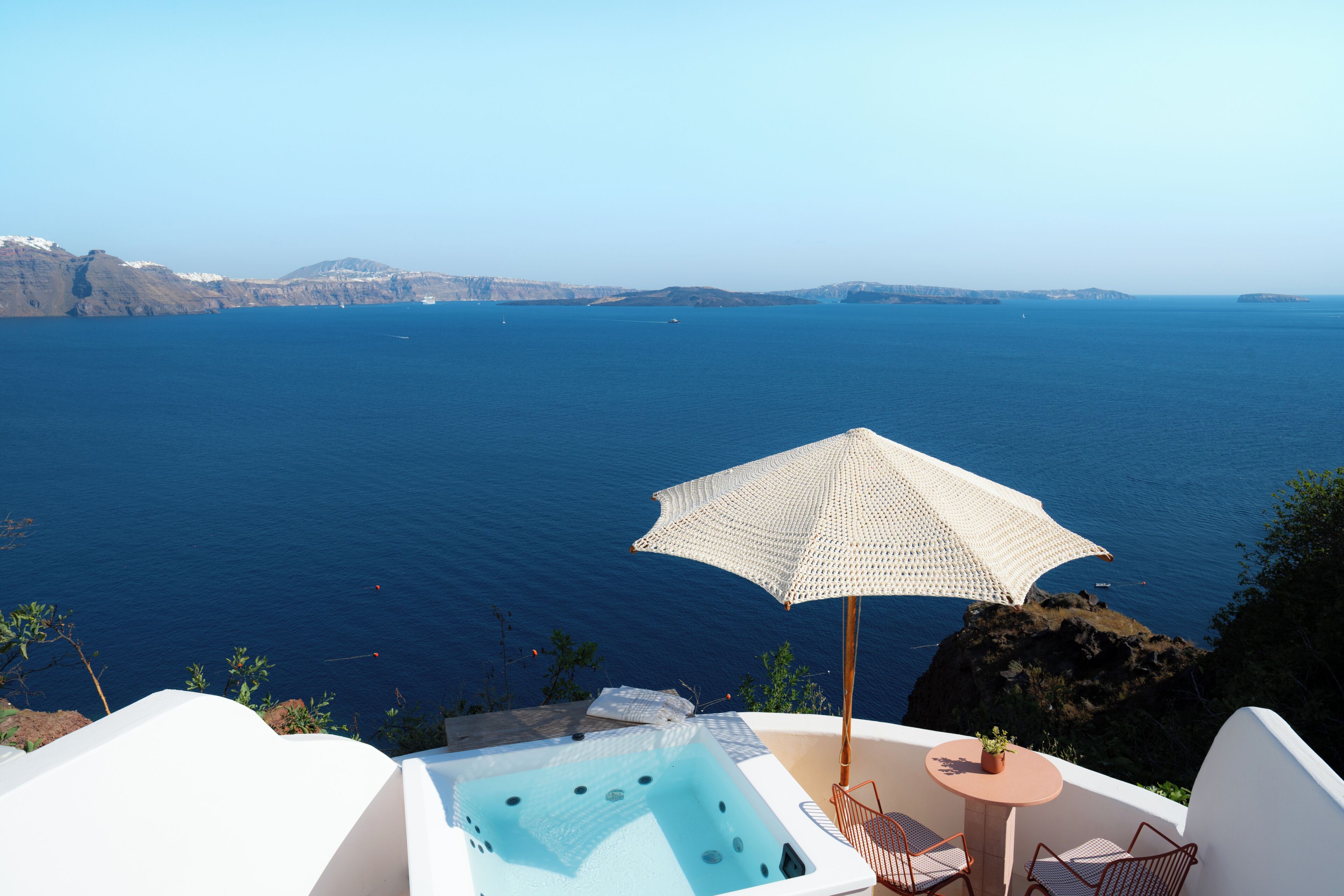 A hot tub with a view of the sea, a table with chairs, and an umbrella.