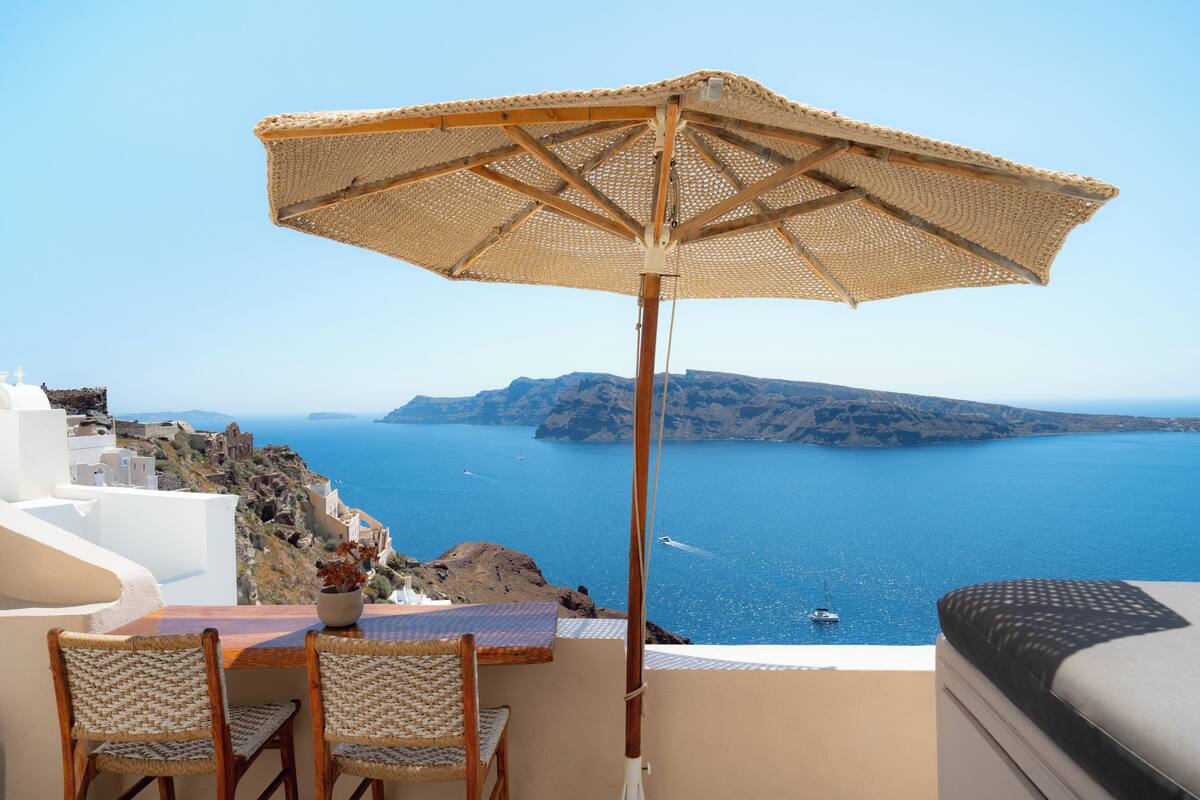 Una mesa con sillas y un parasol de fibra, con vista al mar y un barco a lo lejos.