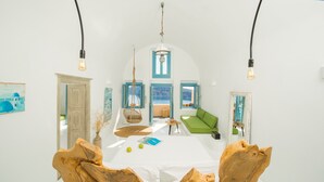 A bright, airy room with a white table, a green sofa, and a view of the sea through a window.