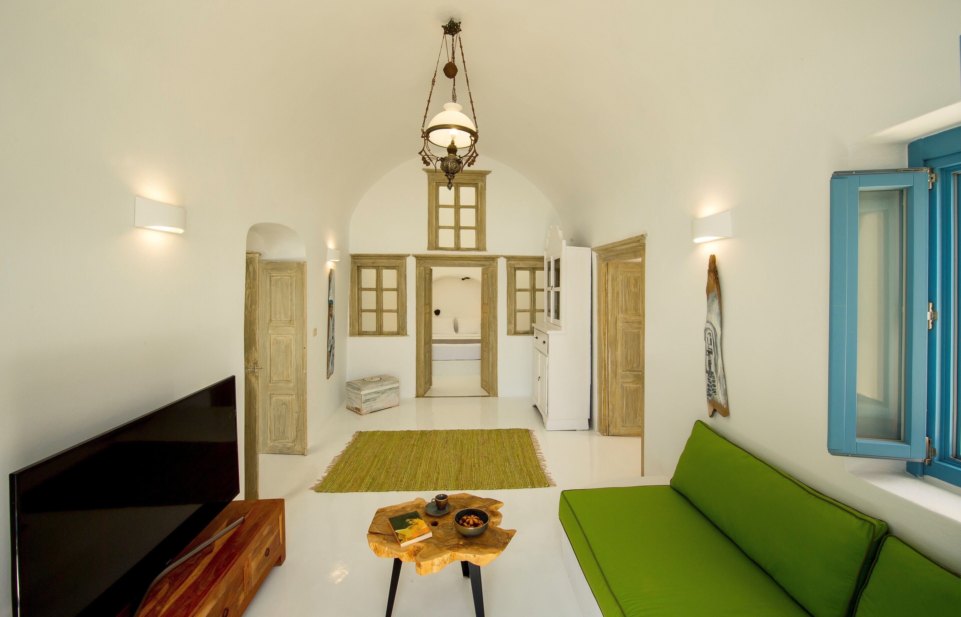 A spacious living room with a flat-screen TV, a wooden coffee table, a green sofa, and a large arched doorway leading to a kitchen area.