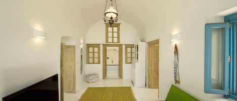 A spacious living room with a flat-screen TV, a wooden coffee table, a green sofa, and a large arched doorway leading to a kitchen area.