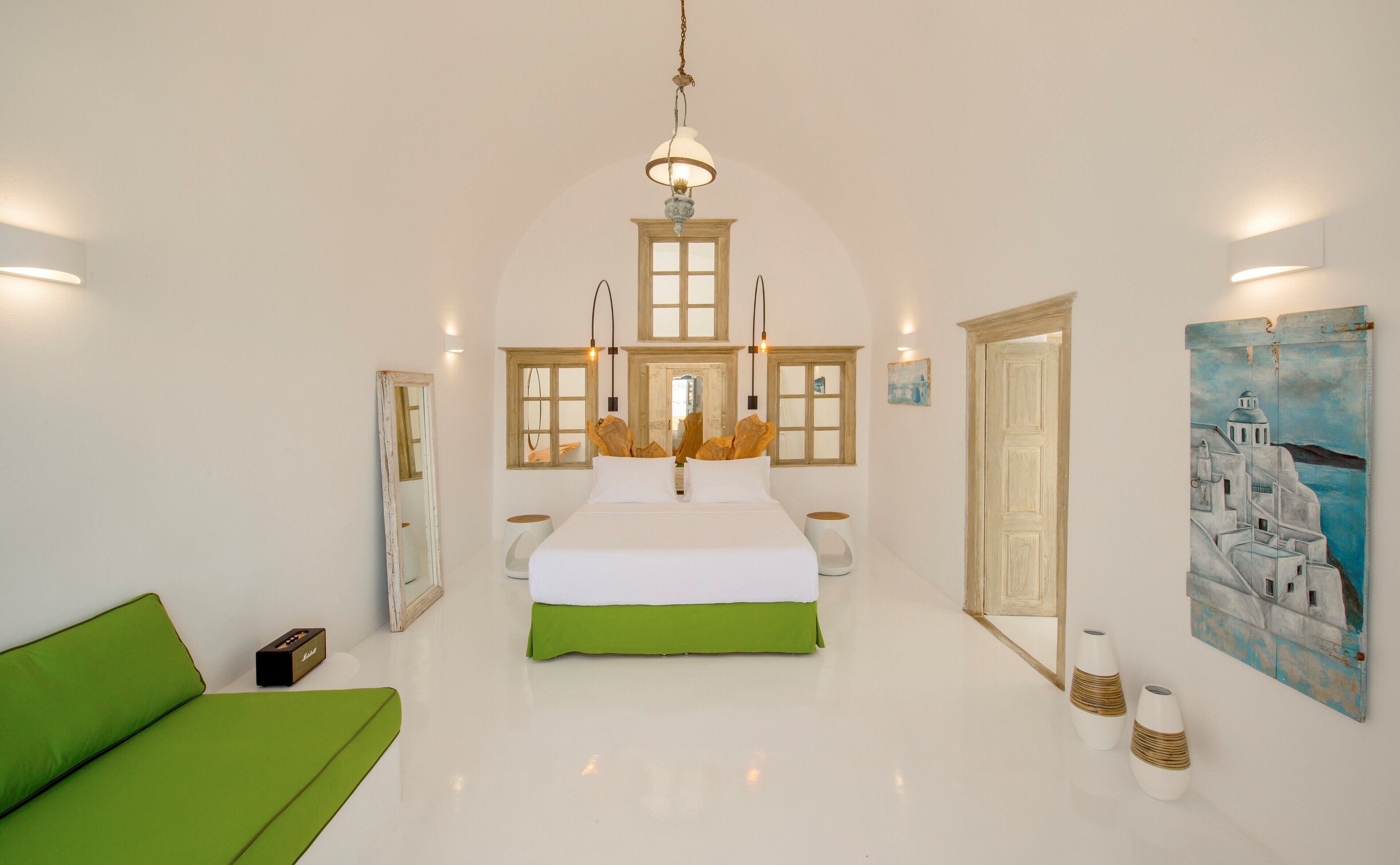 Une chambre spacieuse avec un grand lit, un canapé vert et un tableau représentant un paysage côtier.