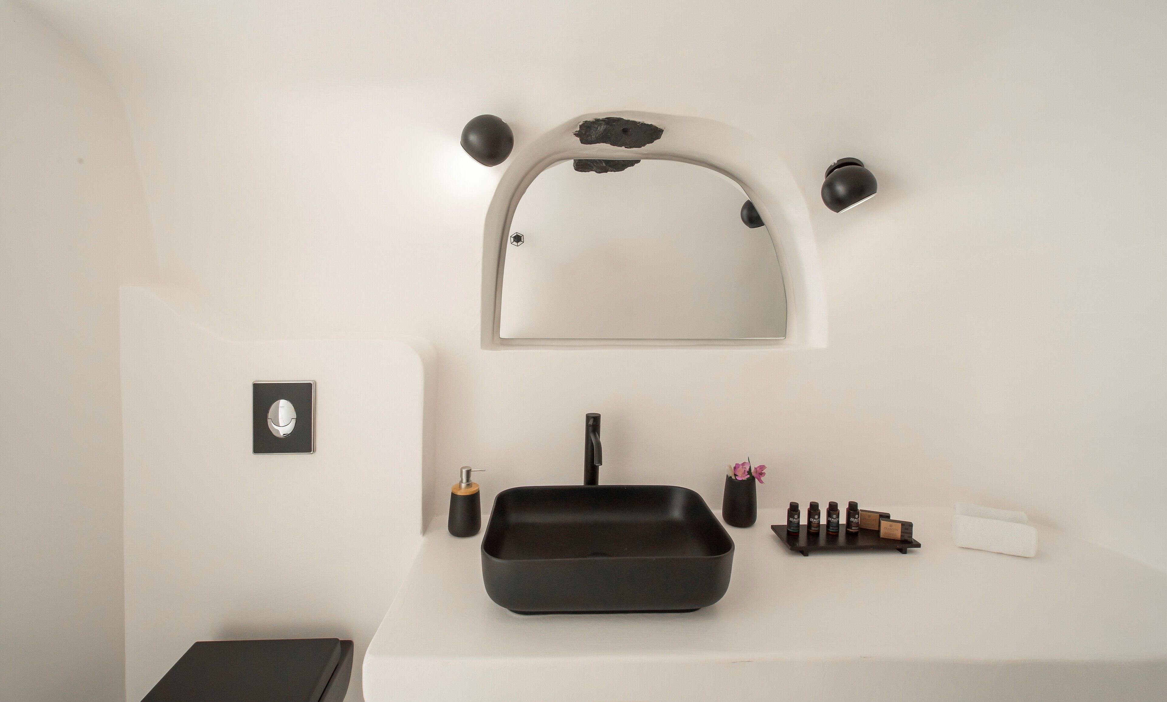 A bathroom with a white sink, black faucet, and a black tray. There is a mirror above the sink with two black wall sconces.