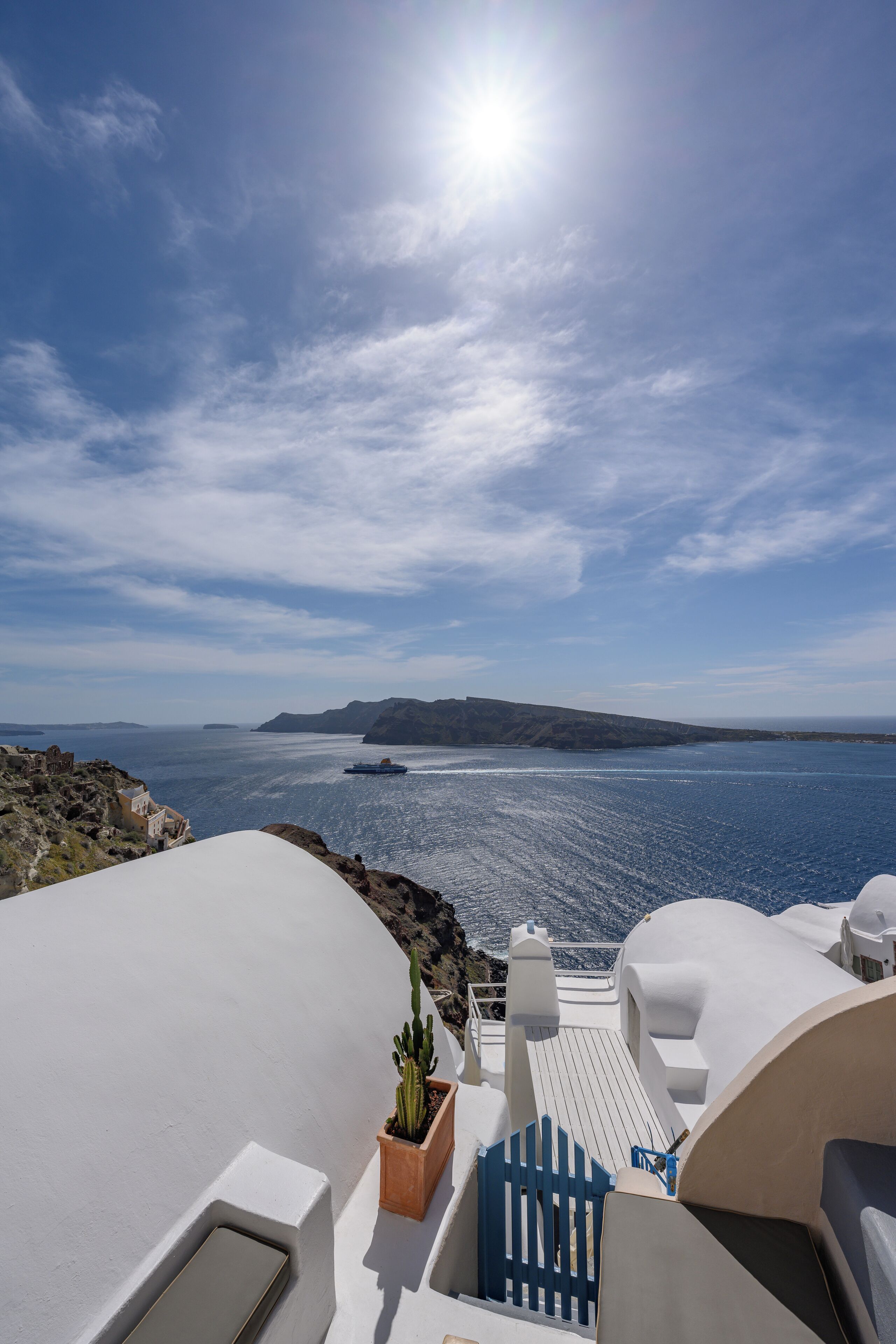 Vista al mar con cielo despejado, un barco en el agua y un edificio blanco con puerta azul.