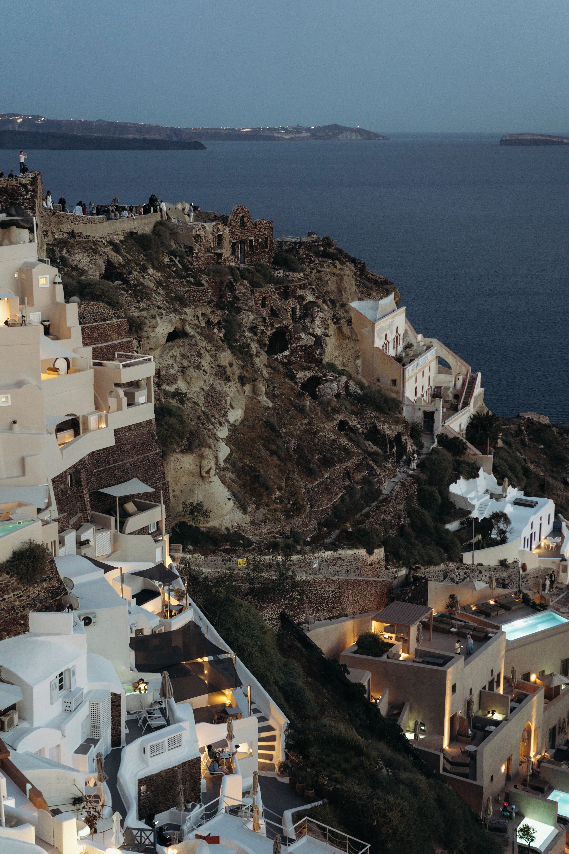 A coastal town with white buildings, a rocky hillside, and a view of the sea.