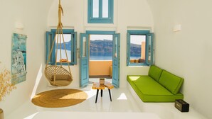 A room with a green sofa, a hanging chair, and a view of the sea through open doors.