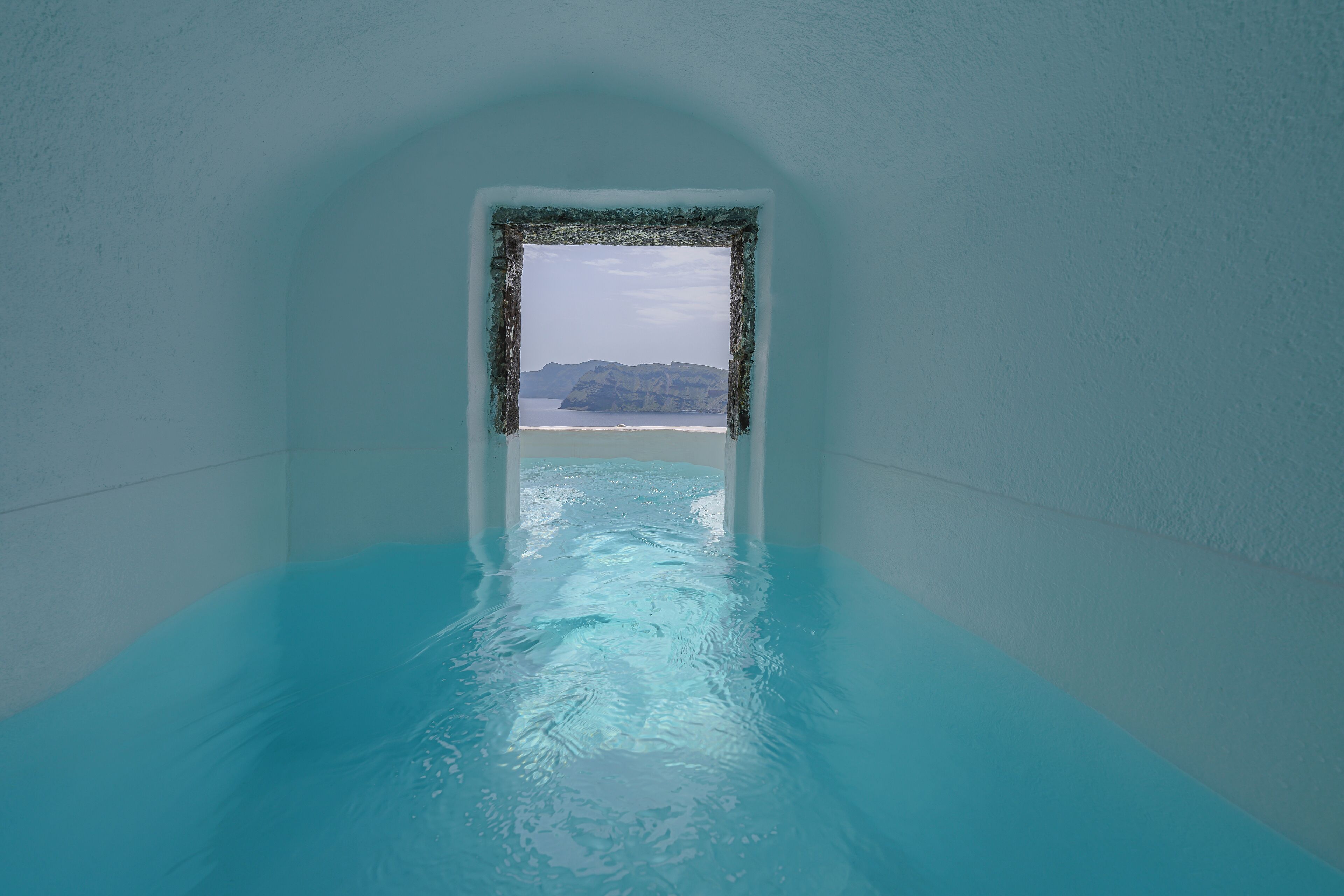 A narrow, icy passage leading to a pool with a view of distant landforms.