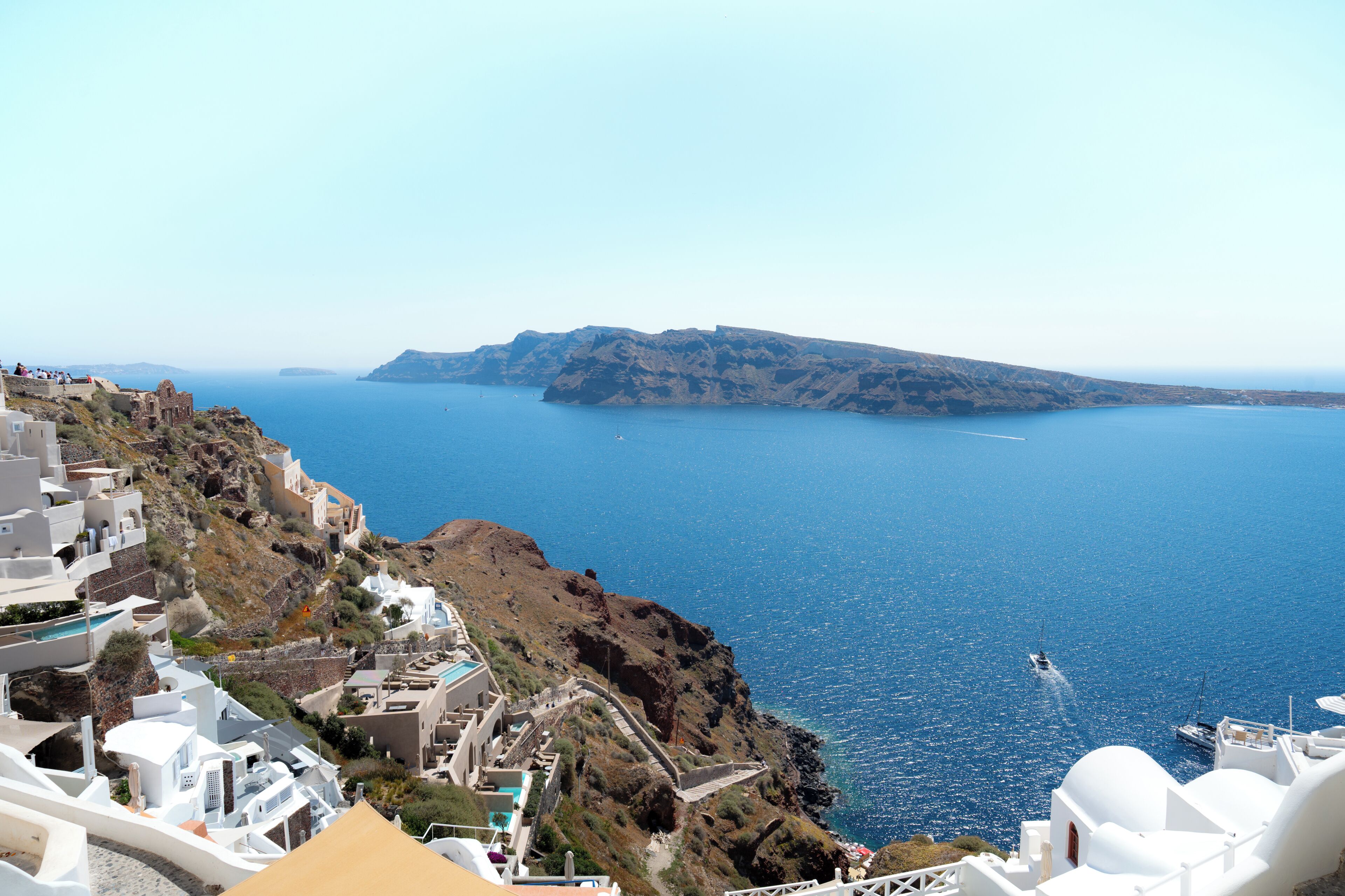 A coastal town with white buildings, a clear blue sea, and a boat in the distance.