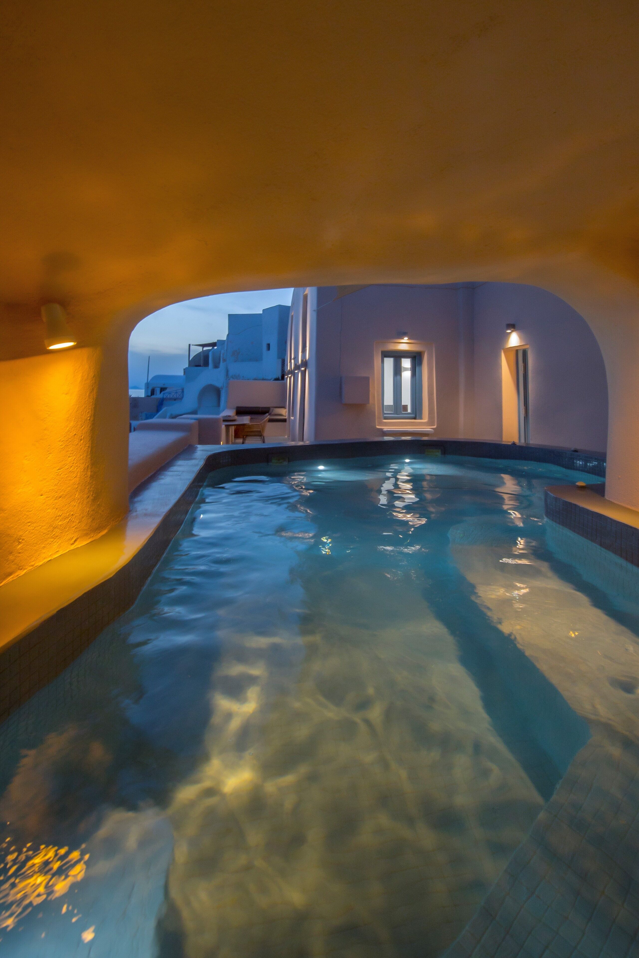 An indoor swimming pool with clear water, surrounded by walls and a door leading outside.