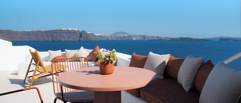 Ein runder Tisch mit Stühlen und einer Couch, eine Topfpflanze und Blick auf das Meer und die Klippen.